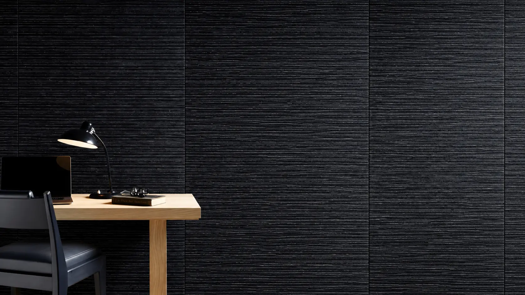 Dark woven wallcovering behind a timber desk and black task lamp.