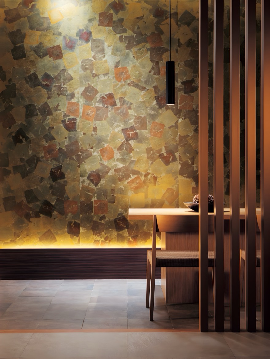 A wall of many-coloured leaf, lit from below, beside a dining table behind wooden slats